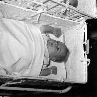 Infant lying in a quilted white bassinet.