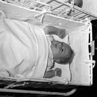 Infant lying in a quilted white bassinet.