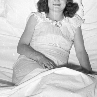 Woman in ruffled dress reclining on white pillows.