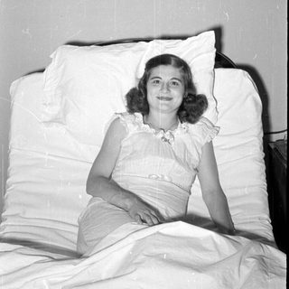 Woman in ruffled dress reclining on white pillows.