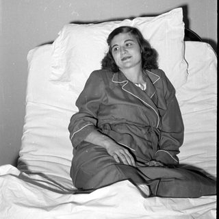 Woman in pajamas reclining on white pillows.