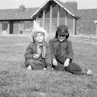 Two children in winter clothes sitting before a house.