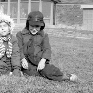 Two children in winter clothes sitting before a house.