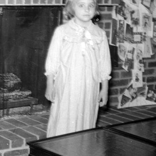 Girl in a dress standing by a brick fireplace.