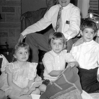 Three children and a man indoors with a gift.