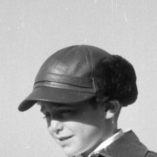 Child in fringed leather jacket and cap.