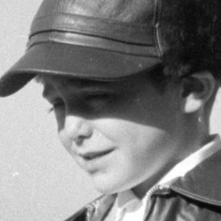 Child in fringed leather jacket and cap.