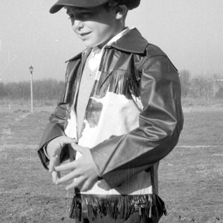 Child in fringed leather jacket and cap.