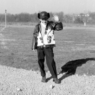 Person in fringed jacket waving in a field.