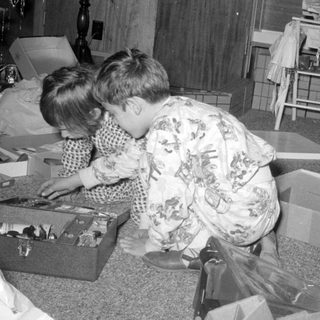 Two children opening presents on a carpeted floor.