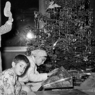 Three children in pajamas by a Christmas tree.
