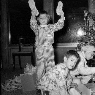 Three children in pajamas by a Christmas tree.