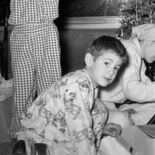 Three children in pajamas by a Christmas tree.
