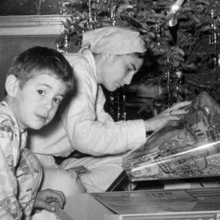 Three children in pajamas by a Christmas tree.