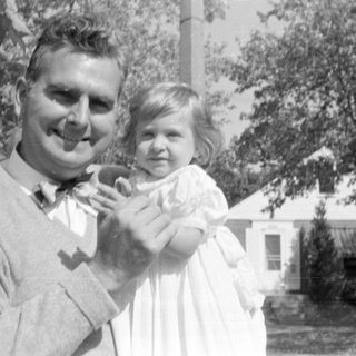 Man and young girl in white dress outdoors.