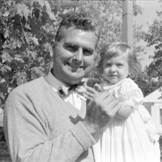Man and young girl in white dress outdoors.