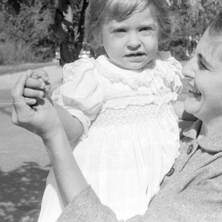 Woman holding a young child in a white dress.
