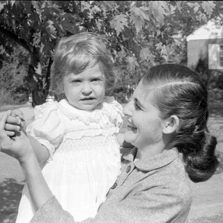 Woman holding a young child in a white dress.