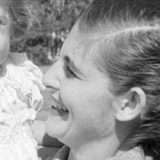 Woman holding a young child in a white dress.