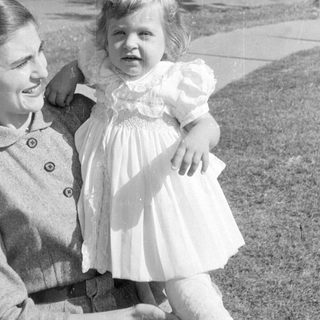 Woman holding a child in a ruffled dress.