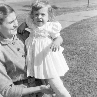Woman holding a child in a ruffled dress.