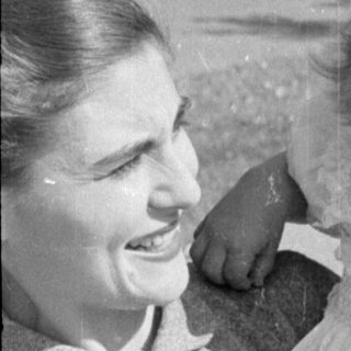 Woman holding a child in a ruffled dress.
