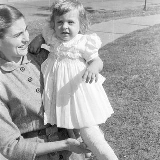 Woman holding a child in a ruffled dress.