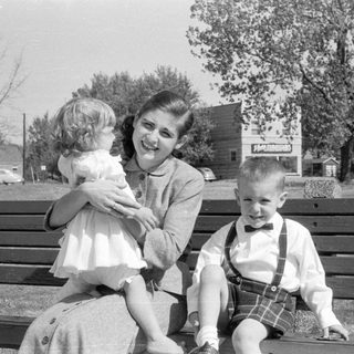 Woman and two children on a wooden park bench.