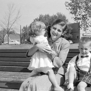 Woman and two children on a wooden park bench.