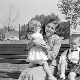 Woman and two children on a wooden park bench.