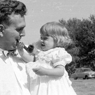 Man and young girl with a pipe outdoors.