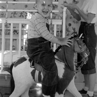 Child on toy horse with girl in background.
