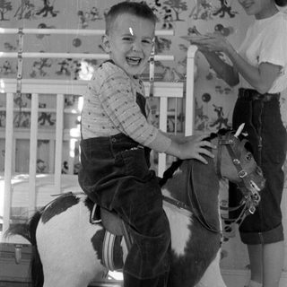 Child on toy horse with girl in background.