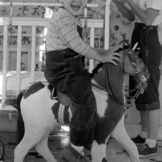 Child on toy horse with girl in background.