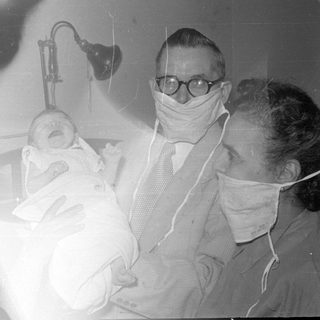 Two masked adults with a newborn baby.