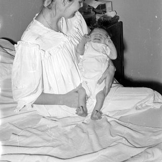 Woman in white dress holding an infant on a bed.