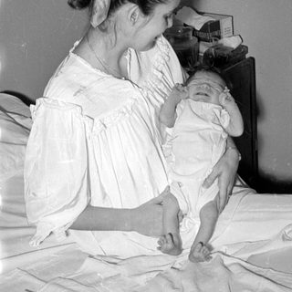 Woman in white dress holding an infant on a bed.
