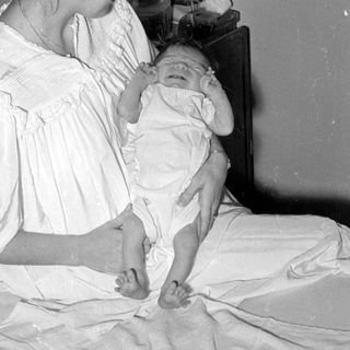 Woman in white dress holding an infant on a bed.