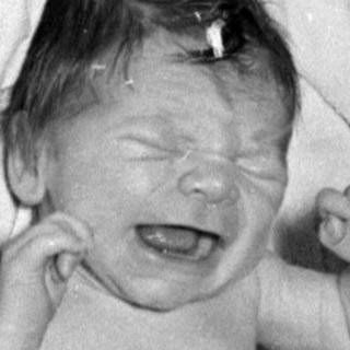 Crying infant in a diaper on white linens.