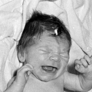 Crying infant in a diaper on white linens.