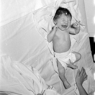 Crying infant in a diaper on white linens.