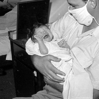 Man in surgical mask holding a crying infant.