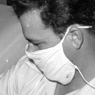 Man in surgical mask holding a crying infant.