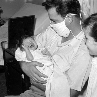 Man in surgical mask holding a crying infant.