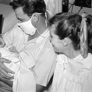Man in surgical mask holding a crying infant.