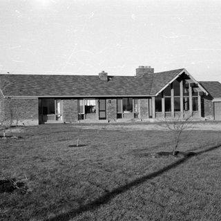 Single-story brick house with large windows on grassy lot.