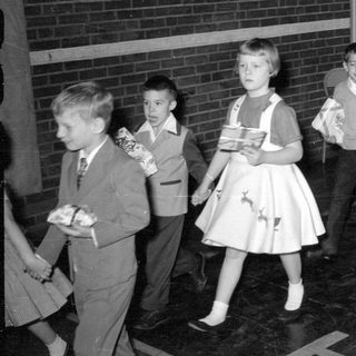 Children in formal wear carrying wrapped gifts.