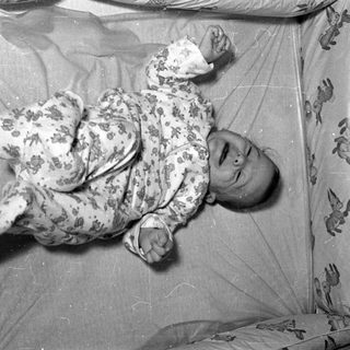 Infant in floral pajamas lying in a crib.
