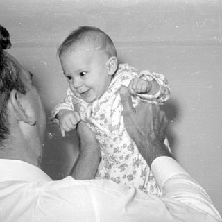 Man holding a baby in a patterned sleeper.