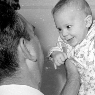 Man holding a baby in a patterned sleeper.